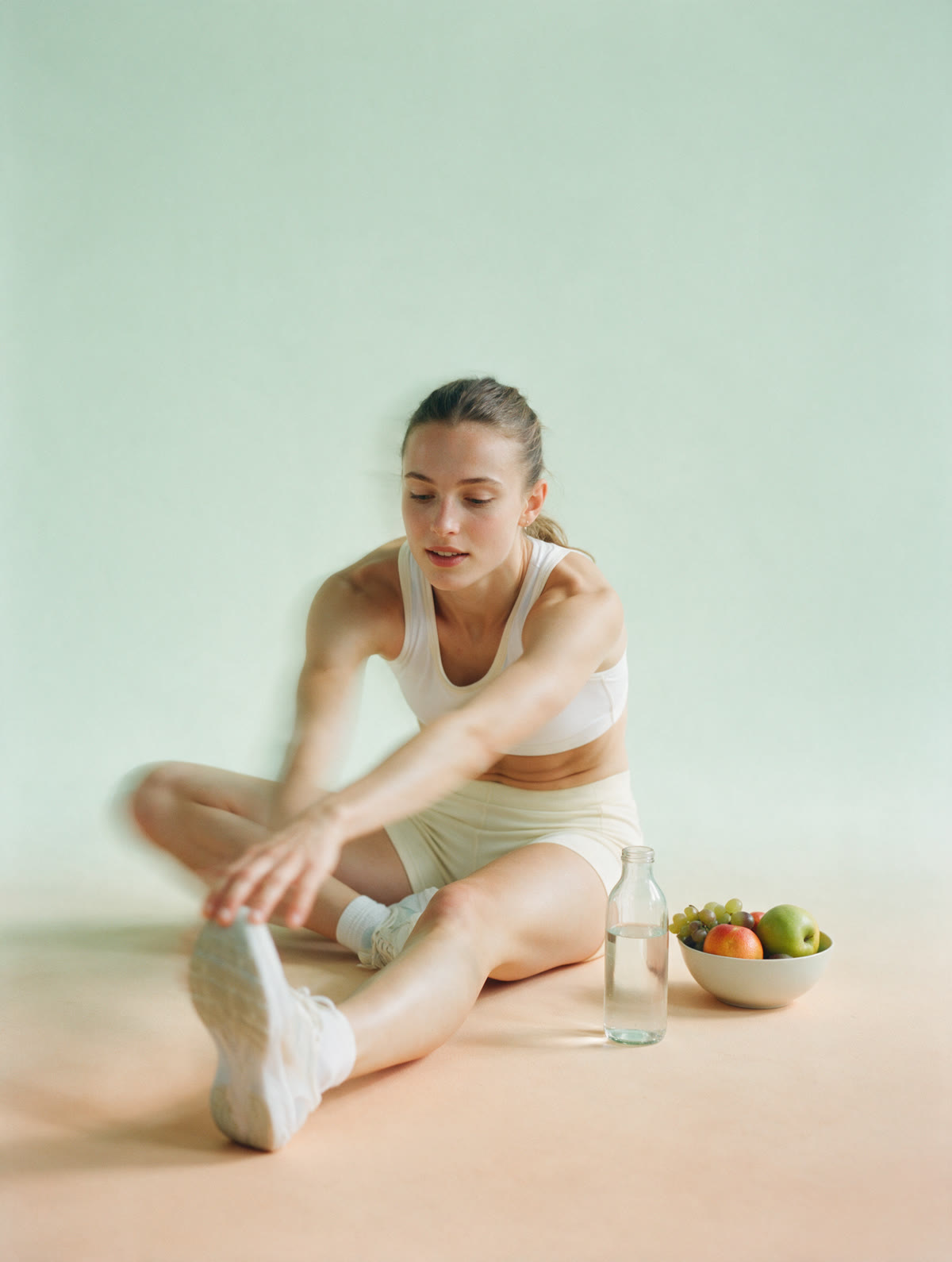 Sprinterin beim Dehnen, Wasserflasche und Obst neben ihr